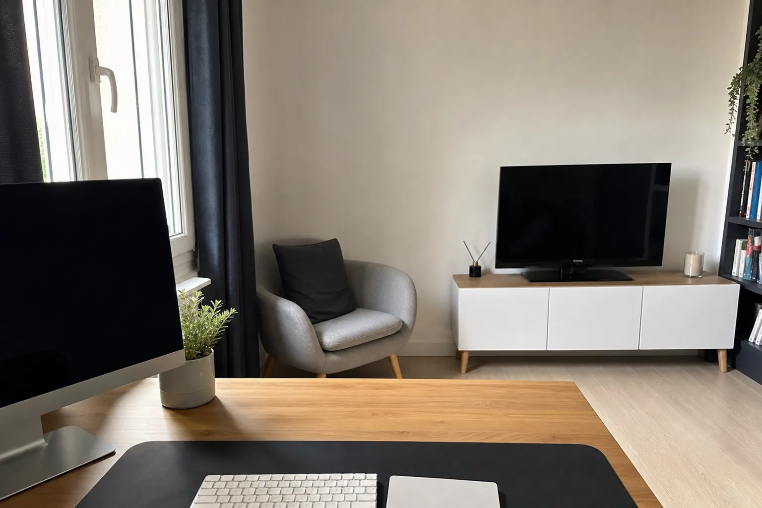 Bureau placé perpendiculairement à une fenêtre dans un séjour, avec un rideau qui filtre la lumière.