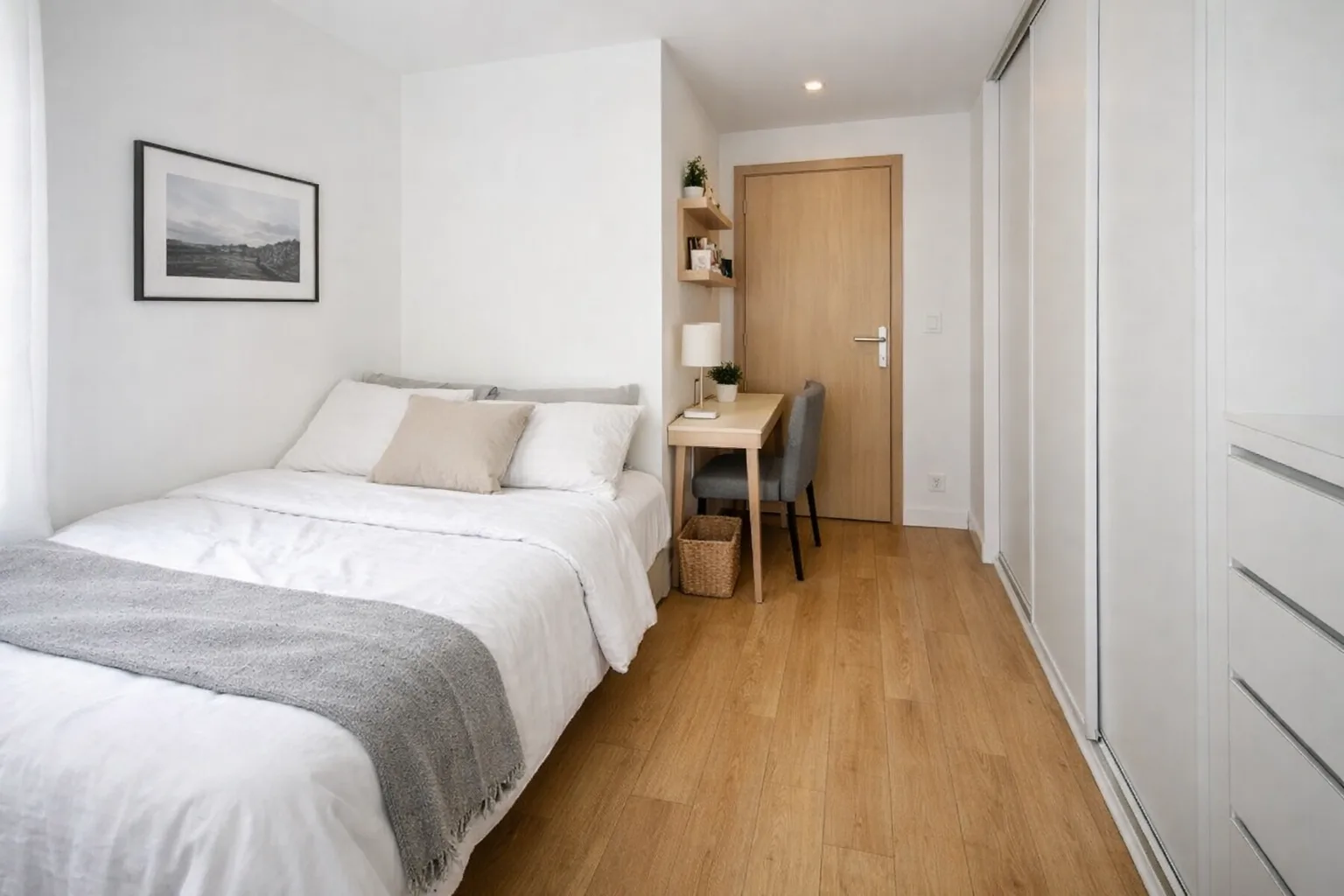 Lit décalé contre un mur dans une chambre étroite, avec un passage libre sur le côté et une armoire près de la porte.
