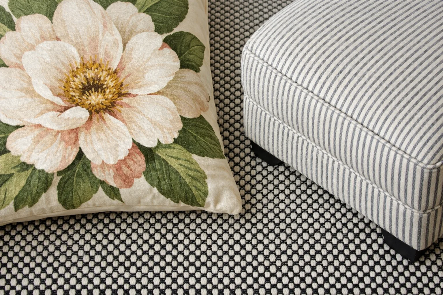 Un coussin à grandes fleurs, une assise à fines rayures et un tapis à petits motifs vus ensemble.